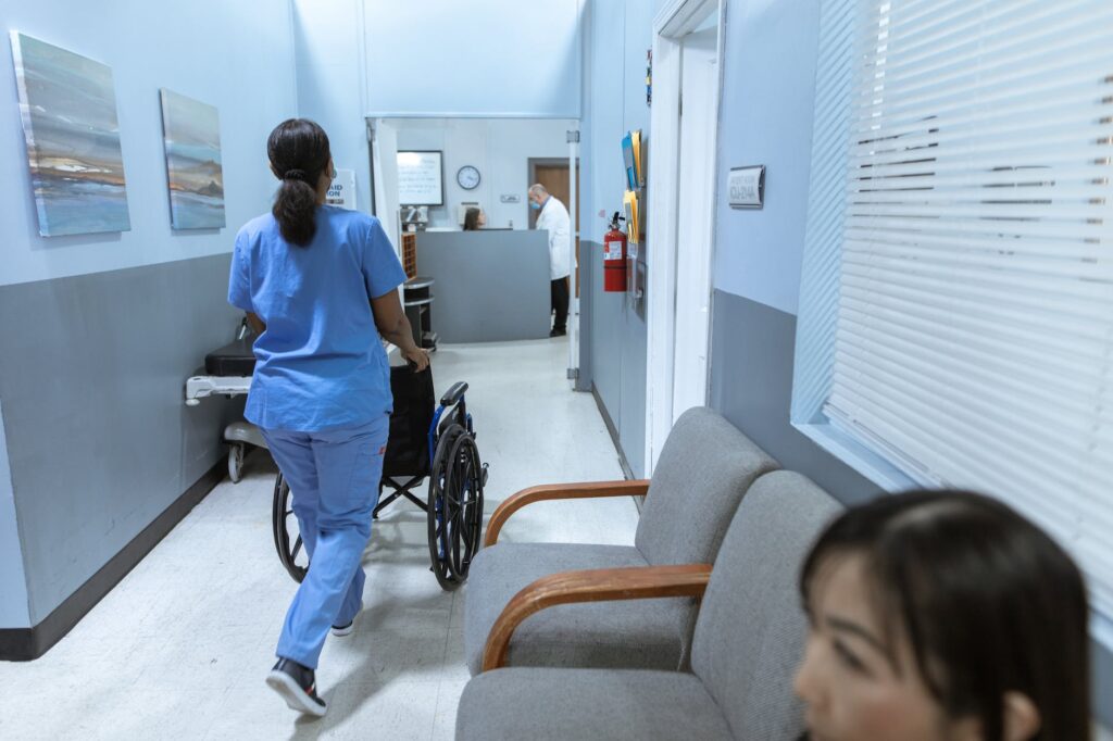 sjuksköterska skjuter en rullstol på sjukhuskorridoren